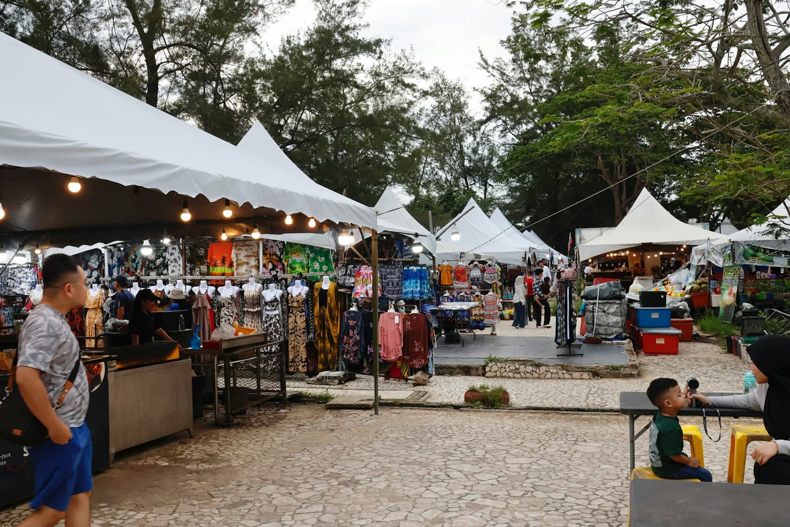 Shoppers browsing an outdoor market lined with white tents